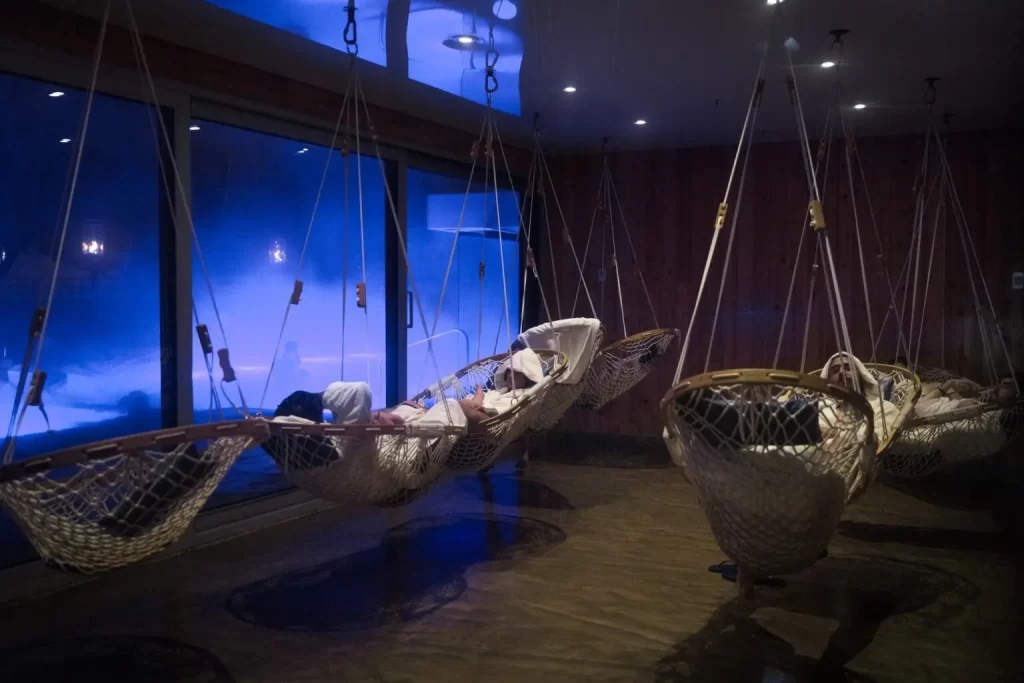Nine individuals all knapping in Cobble Mountain Original Hammock chairs while visiting a Spa. The Cobble Mountain Original Hammock Chairs are hung in a room behind large glass sliding doors.