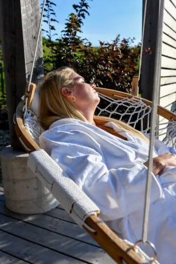 A lady wearing a white bathrobe resting in a Cobble Mountain Summit Hammock Chair basking in the sun