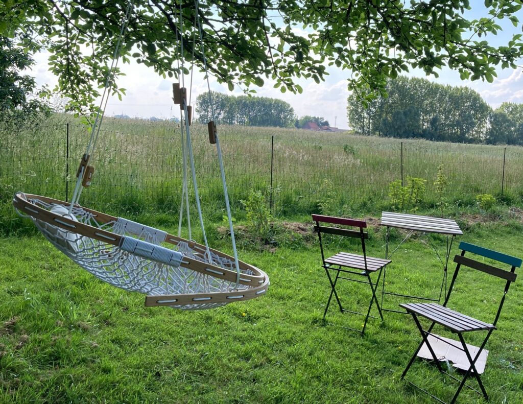 a serene outdoor space. A Cobble Mountain Hammock chair hanging under a tree in a field next to a table and two chairs.