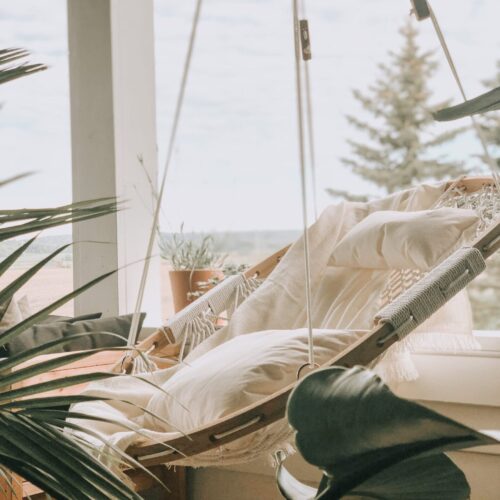 Cobble Mountain Summit Hammock Chair hanging on a porch with white pillows and a white blanket draped over it.
