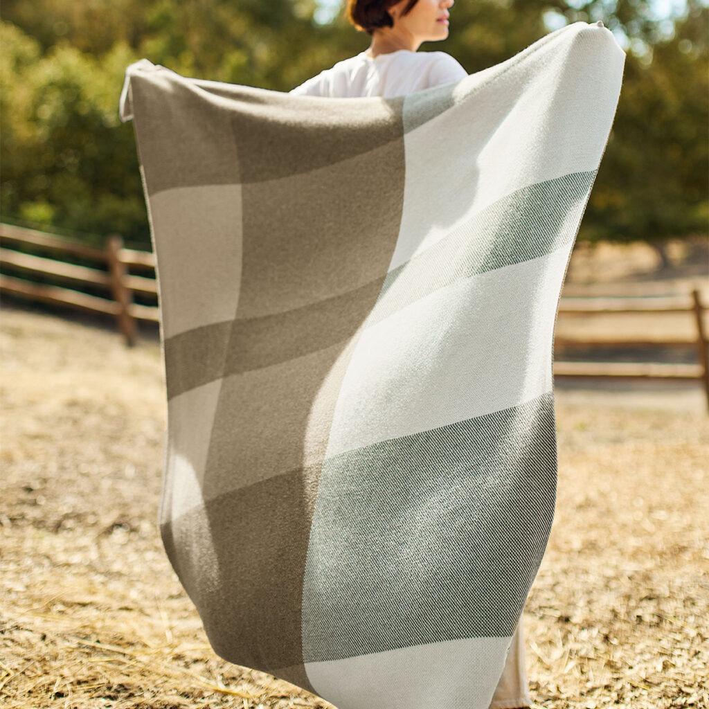 Sunbrella plaid indoor outdoor throw blanket being held stretched out behind person.